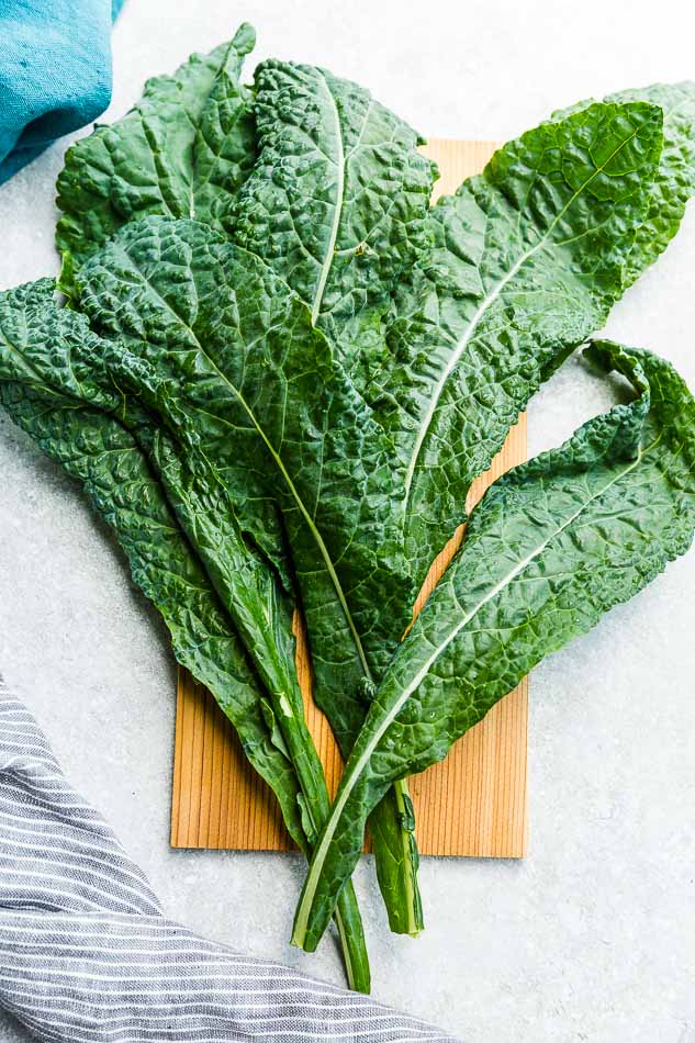 Top view of kale leaves on a wooden board on a grey background