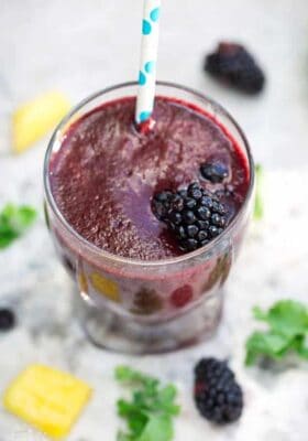 A blackberry kale smoothie in a glass with a blue and white straw and a blackberry on top
