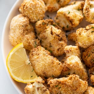Close-up shot of air fryer cauliflower wings with a lemon wedge in a white bowl