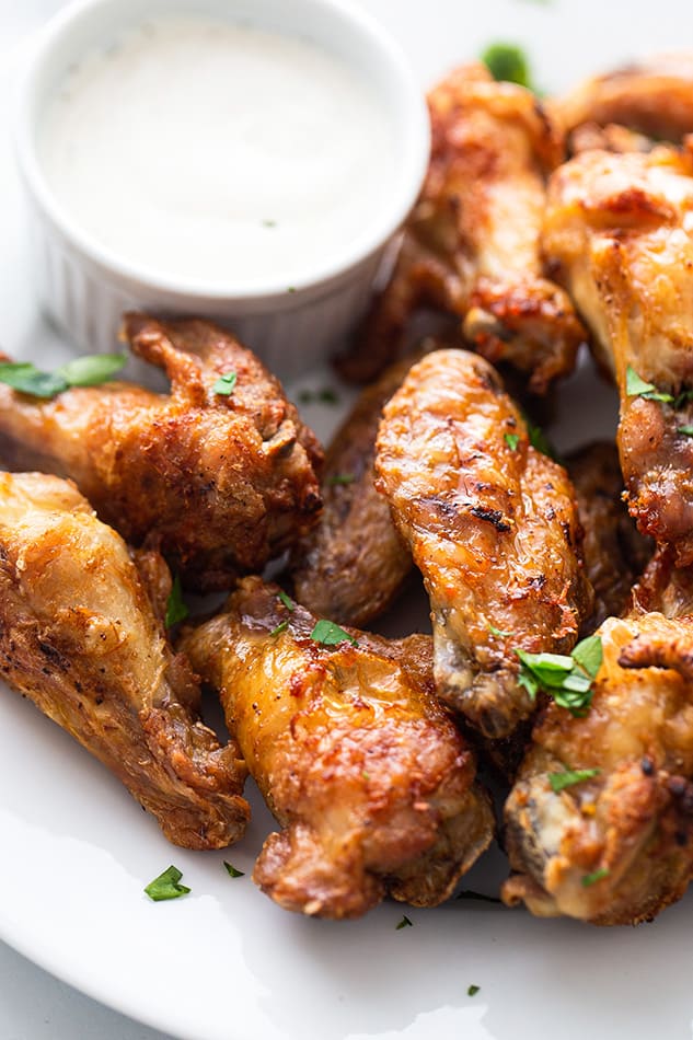 Close-up of crispy Air Fryer Chicken Wings on a white plate with a cup of creamy dipping sauce