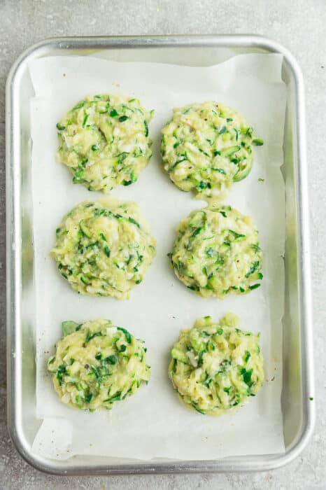 Six unbaked zucchini fritters on a cookie sheet lined with parchment paper