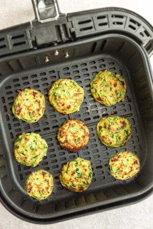 Nine cooked zucchini fritters inside of an Air Fryer basket