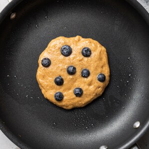 One uncooked blueberry pancake in a black nonstick pan