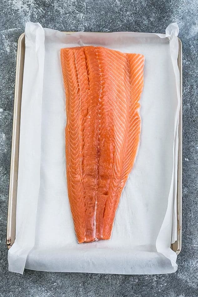 A large uncooked salmon fillet sitting on a parchment-lined baking sheet