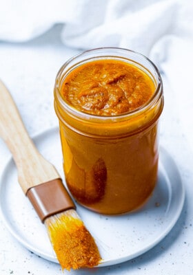 45 degree shot of homemade buffalo sauce in a medium glass jar with a brush