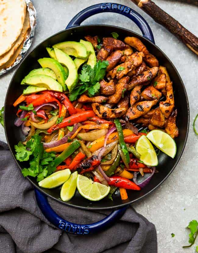 Top view of Keto Chicken Burrito Bowls in a blue skillet with chicken, avocado, bell peppers and lime