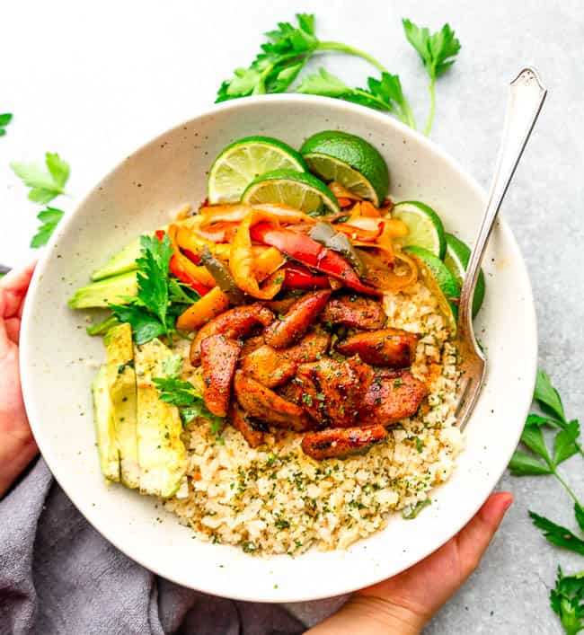 Top view of Keto Chicken Burrito Bowls in a white bowl with cauilfower rice, lime and avocado