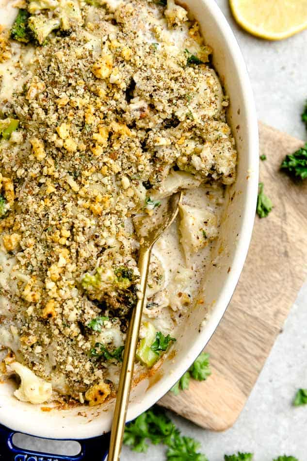 Top close up view of cauliflower gratin in a blue oval casserole dish on a wooden board with a golden spoon