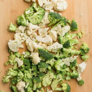 Top view of chopped fresh cauliflower and broccoli florets on a wooden cutting board
