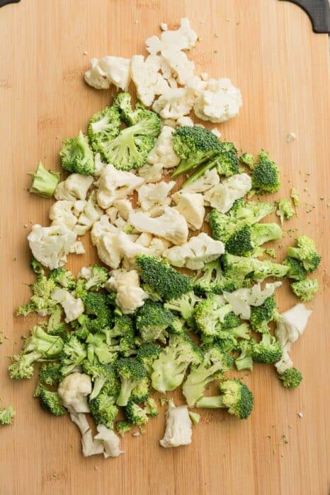 Top view of chopped fresh cauliflower and broccoli florets on a wooden cutting board