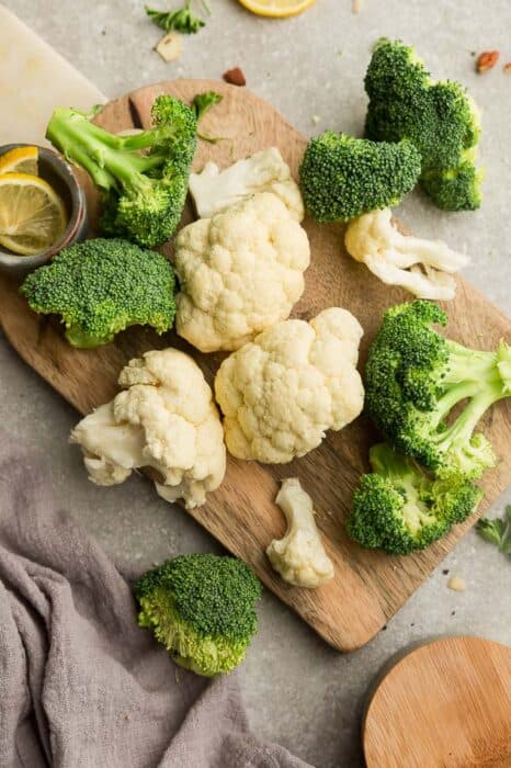 Top view of fresh cauliflower and broccoli florets on a wooden cutting board