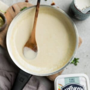 Top view of creamy dairy free sauce in a white skillet with a wooden spoon on a wooden cutting board on a grey background
