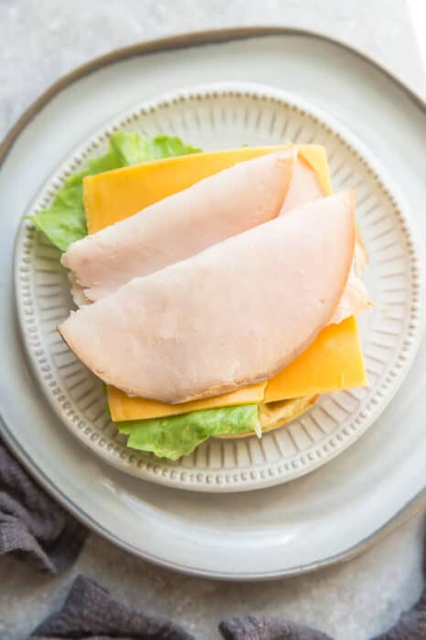Top view of keto chaffle sandwich with lettuce, cheese and turkey on a white plate with a fork on a grey background