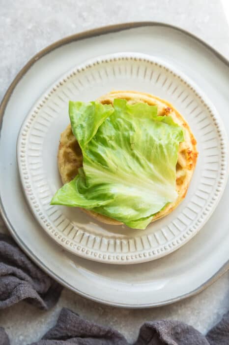 Top view of keto chaffle sandwich on a white plate with a fork on a grey background