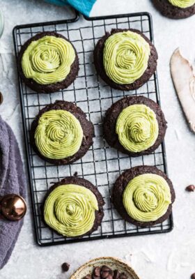 Top view of six keto chocolate fudge cookies with matcha green frosting on a wire rack with chocolate chips on the side