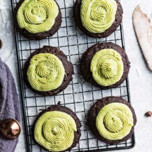 Top view of six keto chocolate fudge cookies with matcha green frosting on a wire rack with chocolate chips on the side