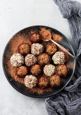 Variety of homemade dark chocolate truffles with cocoa powder, pistachios, almonds in light gray background texture. Top view, copy space.