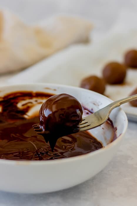 A fork dipping a chocolate truffle into a bowl of melted chocolate