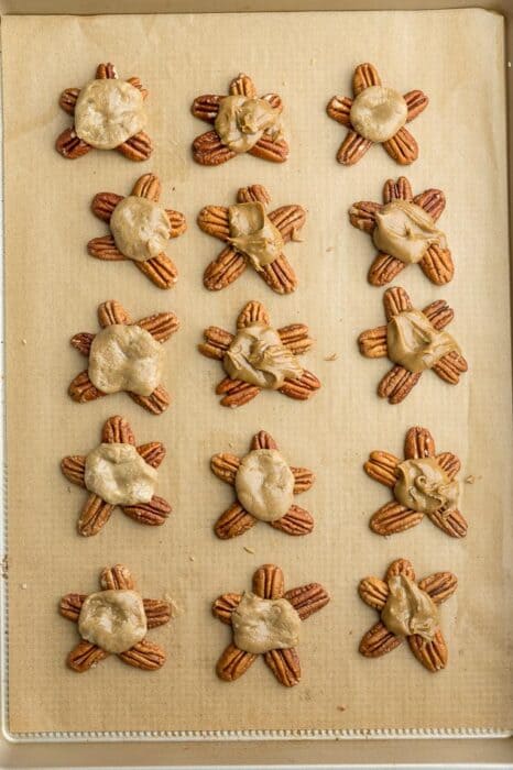 Top view of 15 caramel turtles on a baking sheet with parchment paper