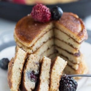 Side view of a stack of fluffy coconut flour pancakes on a plate with berries on a grey background