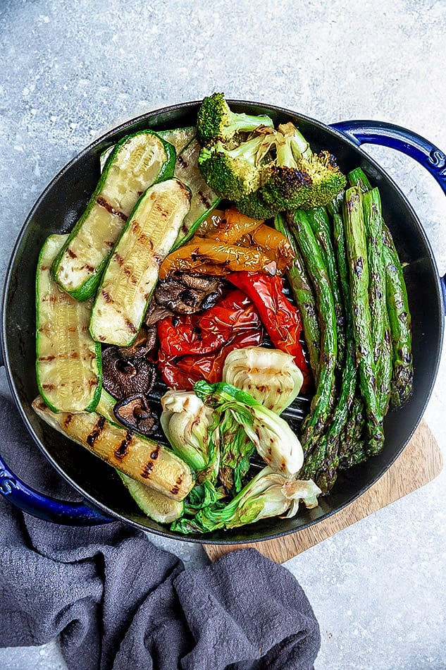 Top view of grilled vegetables in dark bowl on grey surface.