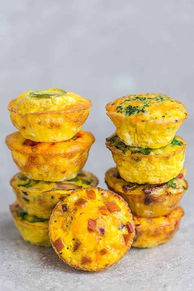 Two Stacks of Breakfast Egg Muffins of Various Flavors with a Ham and Cheese Muffin in the Front