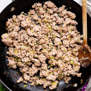 Crumbled brown ground turkey in a black wok with a wooden spoon