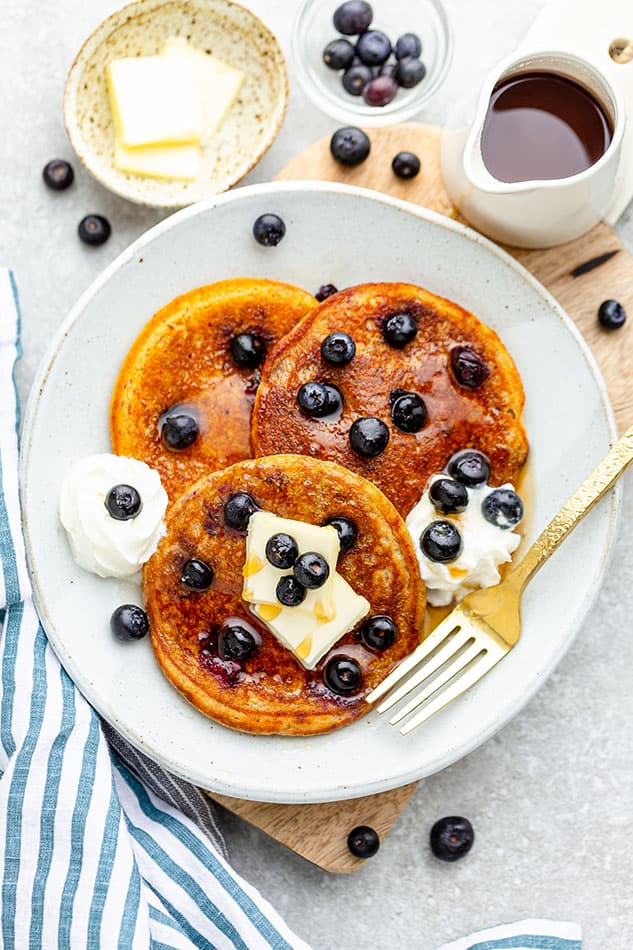 Three fluffy Keto blueberry pancakes on a white plate with a golden fork