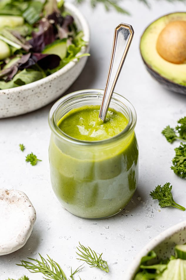 45 degree shot of green goddess dressing in a small jar with a spoon