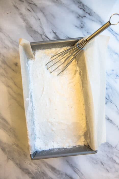 Top view of half-frozen Low Carb Keto Ice Cream in a loaf pan lined with parchment paper and a whisk