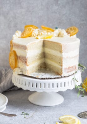 Side view of one low carb lemon cake on a white cake stand with one slice cut out