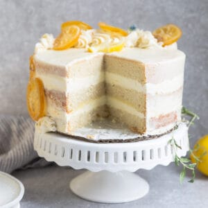 Side view of one low carb lemon cake on a white cake stand with one slice cut out
