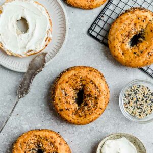 Top view of four Low Carb Keto Bagels with everything bagel seasoning on a grey backgroundwith cream cheese and a knife