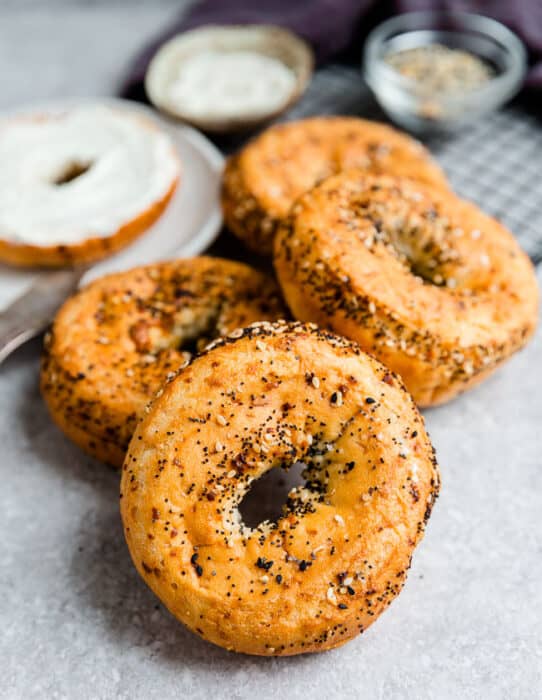 Side view of four Low Carb Keto Bagels with everything bagel seasoning on a grey background with one slice topped with cream cheese