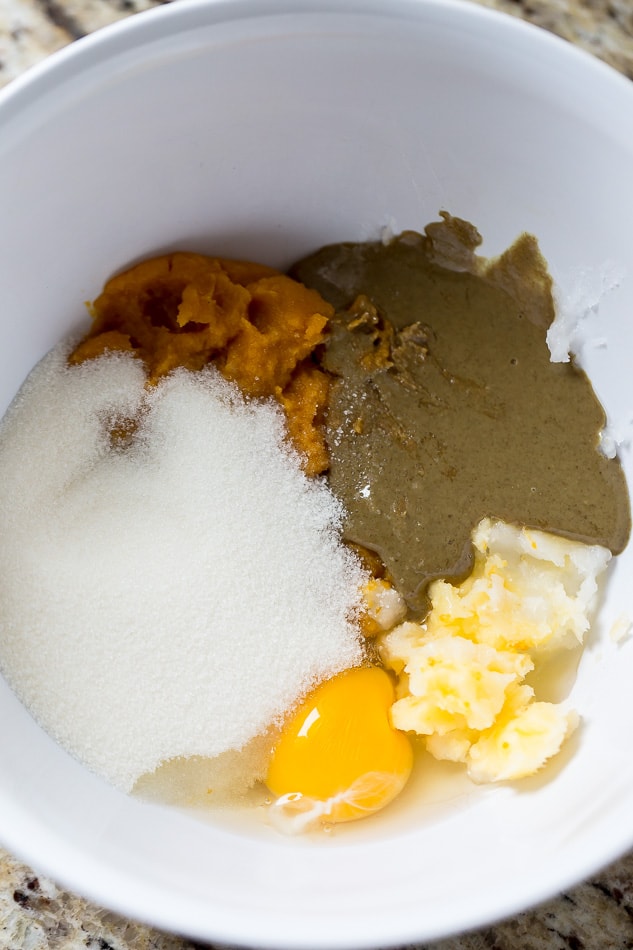 Canned pumpkin, coconut cream, pumpkin seed butter, maple sugar, eggs, and spices in a white mixing bowl