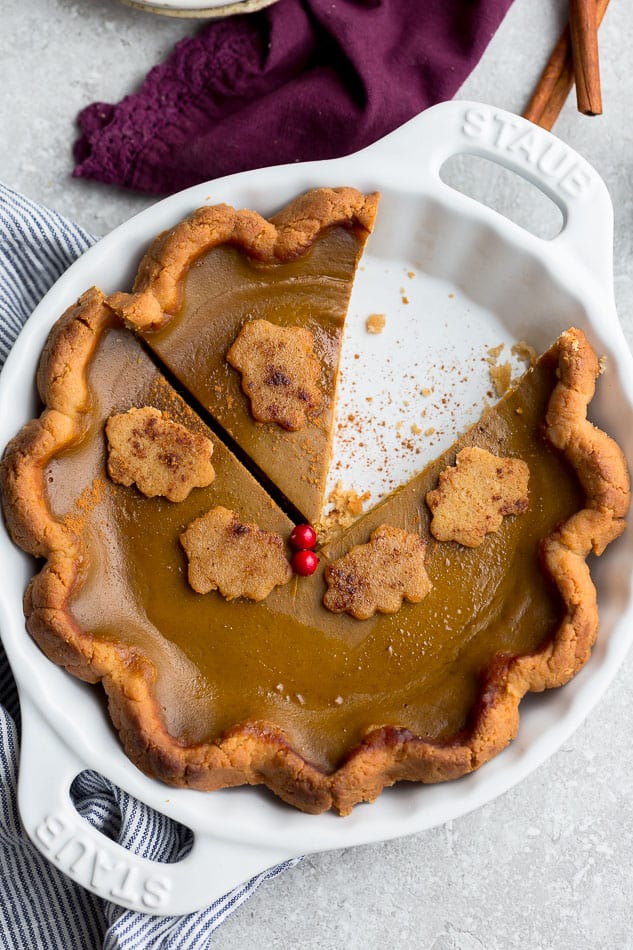 Overhead view of a pumpkin pie in a pie pan, with a slice missing, next to some cinnamon sticks