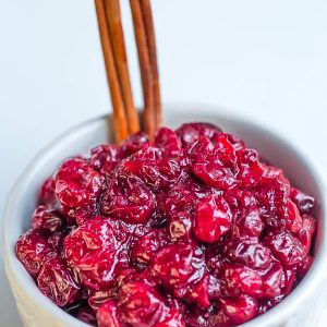 Low carb cranberry sauce in a white bowl with cinnamon sticks