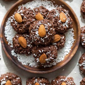 Top view of 6 stacked Low Carb Keto No Bake Cookies in a wooden bowl on a white baking sheet with parchment paper with more cookies