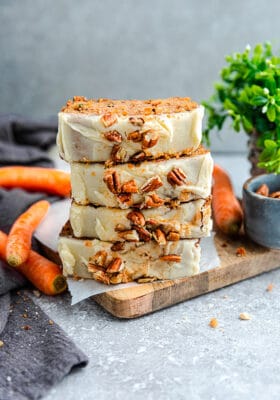 Side view of 4 stacked carrot loaf slices on a wooden cutting board