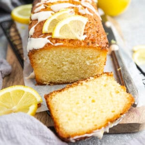 Side view of whole paleo lemon bread with glaze on a grey background with a knife