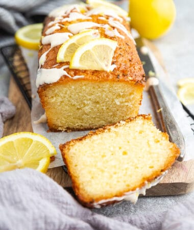 Side view of whole paleo lemon bread with glaze on a grey background with a knife