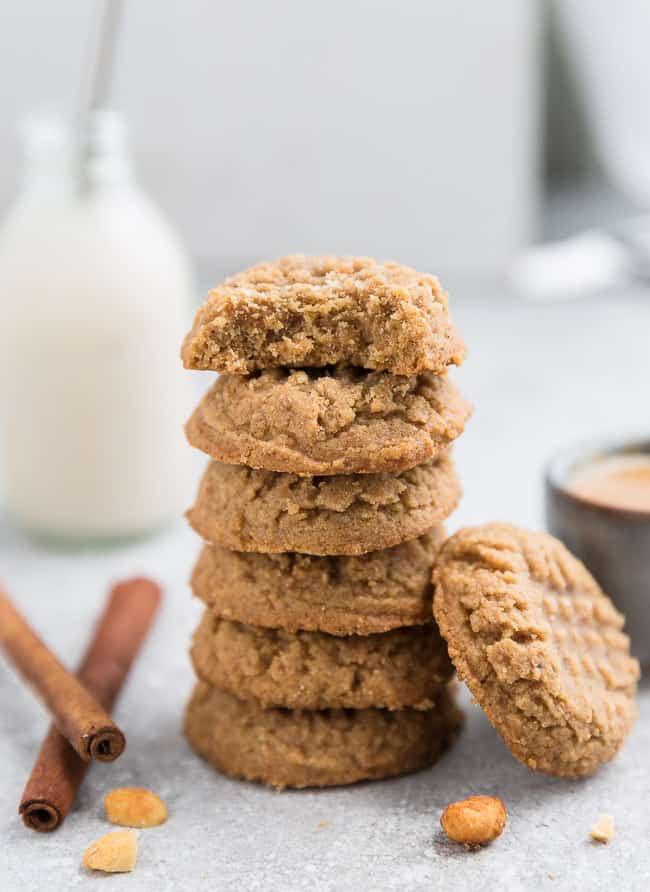 Side view of 5 stacked keto peanut butter cookies with one keto peanut butter cookie with a bite taken on top on a grey background with a milk bottle in the background