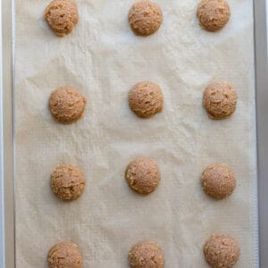 Twelve raw dough balls arranged on a pan lined with parchment paper