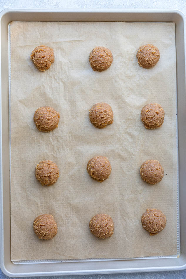Twelve raw dough balls arranged on a pan lined with parchment paper