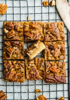 Top view of keto pecan pie bars cut into nine squares on wire rack on a grey backgroud with one flipped on an angle