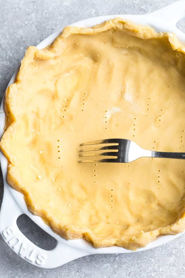 An unbaked pie crust covered in poke marks from a fork, with a fork on it