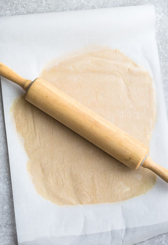 A rolled out piece of pie dough with a sheet of parchment paper on top, with a rolling pin on top of it