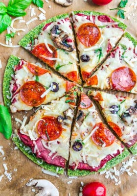 Close-up top view of sliced baked Broccoli Pizza Crust with tomato sauce, cheese, mushrooms, olives and pepperoni on brown parchment paper on a baking sheet