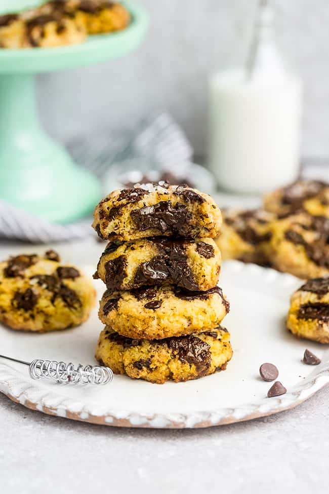 Keto Pumpkin Chocolate Chip Cookies stacked on a plate with milk and a cakeplate in the background