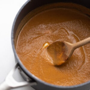 Melted pumpkin puree filling in grey pot with a wooden spoon